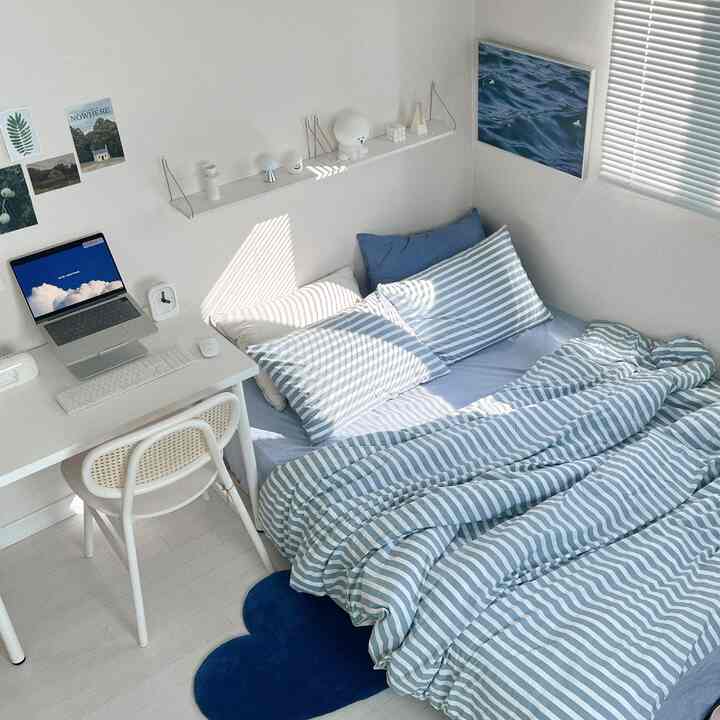 ホワイトとブルーのトーンが特徴的な一人暮らし用寝室、デスクとベッドが配置された居心地の良いコンパクトな空間