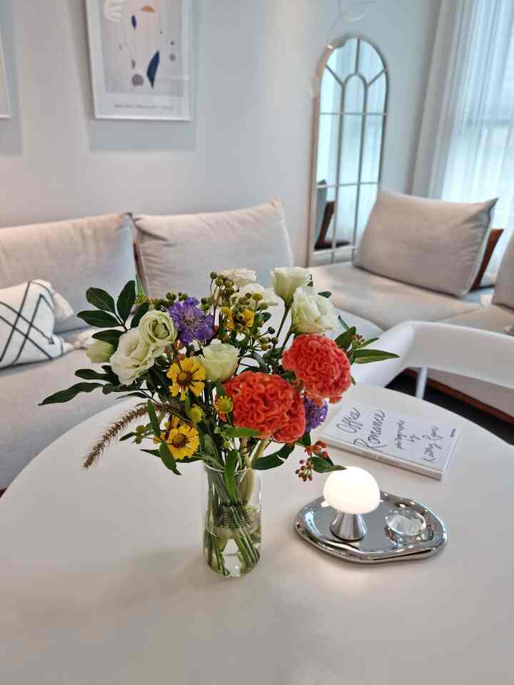 A white and beige toned living room with a vase of colorful flowers and a mini mood lamp on a central table creating a cozy setting