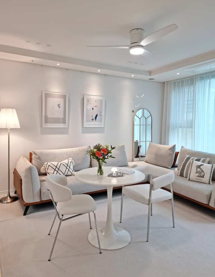 White-toned living room featuring mid-century modern sofas, round table, vase with flowers, and framed art creating a modern atmosphere