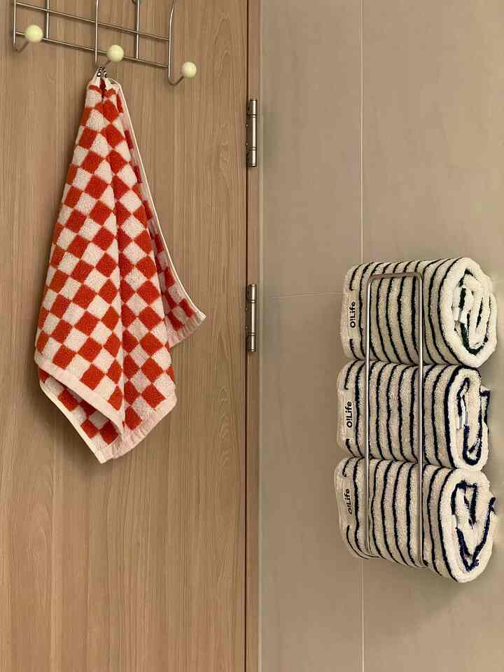 オレンジの格子柄タオルが扉に掛かり、白とネイビーのストライプ柄のホテルタオルが浴室の壁に収納された清潔感のある空間