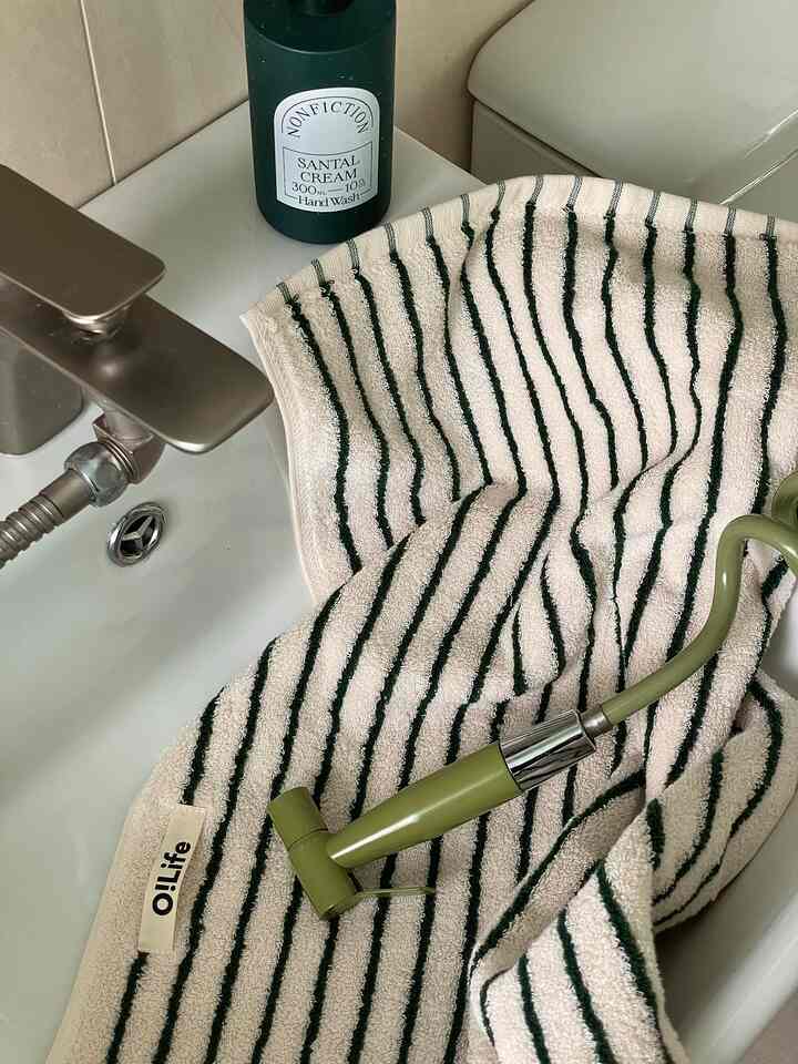 グリーンストライプのタオルとバス用品が配置された清潔感のあるバスルームの雰囲気