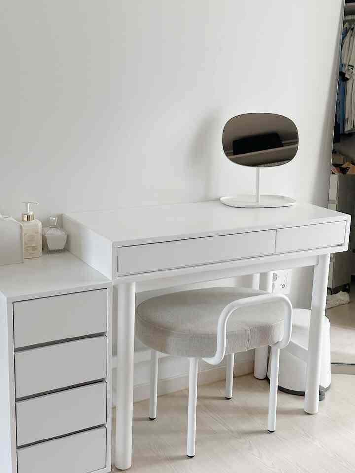 White and natural-toned walk-in closet vanity with mirror and stool in a clean, modern space