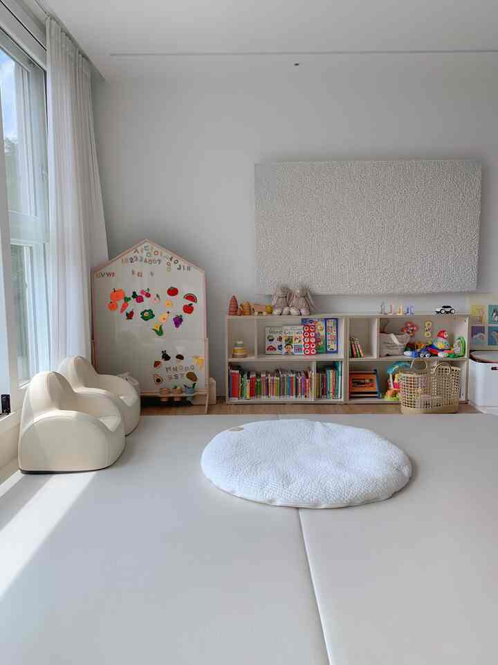 明るいホワイトトーンの赤ちゃんと暮らすリビング、子供用チェアと学習用ボード、玩具収納が配置された温かみのある空間