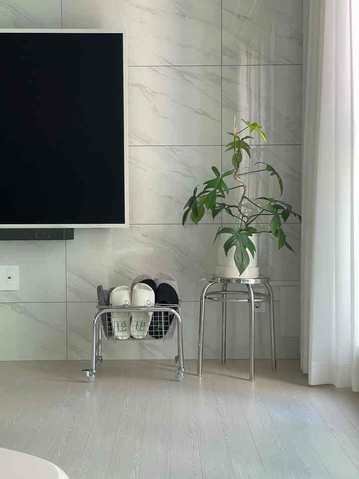 ホワイトの背景にシルバーのスツールと中央右に配置されたグリーンプラントが調和するモダンなリビング空間