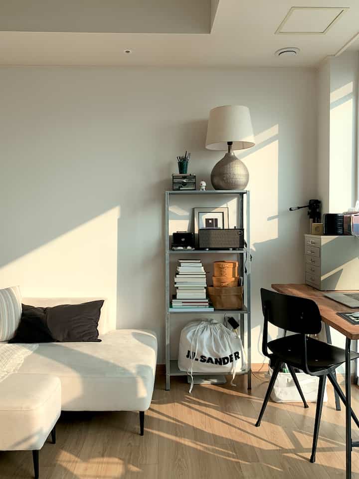 Ivory and wood tone living room with a spacious sofa, metal bookshelf, and wooden desk bathed in natural morning light