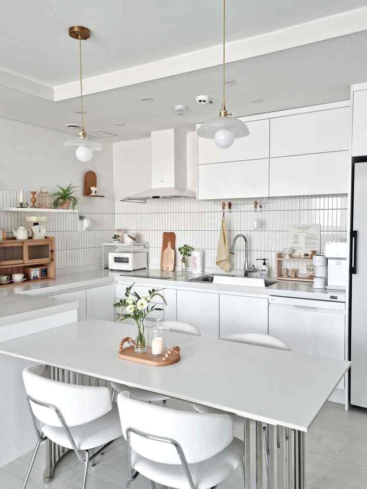 A clean and simple white and wood tone kitchen space featuring a dining table set and pendant lights