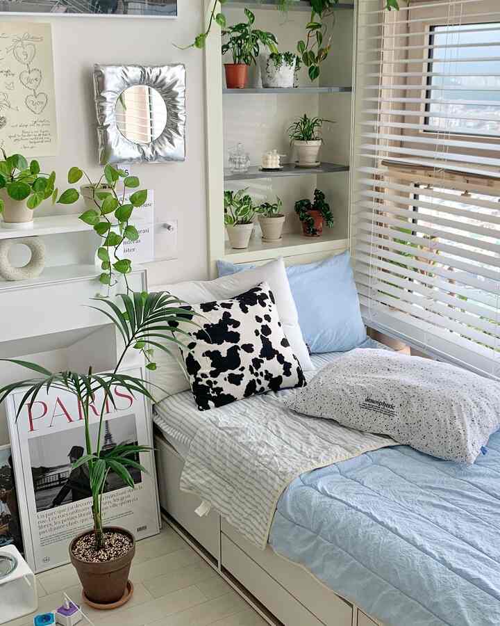 White and green toned studio bedroom featuring a storage bed and multiple plants creating a cozy atmosphere