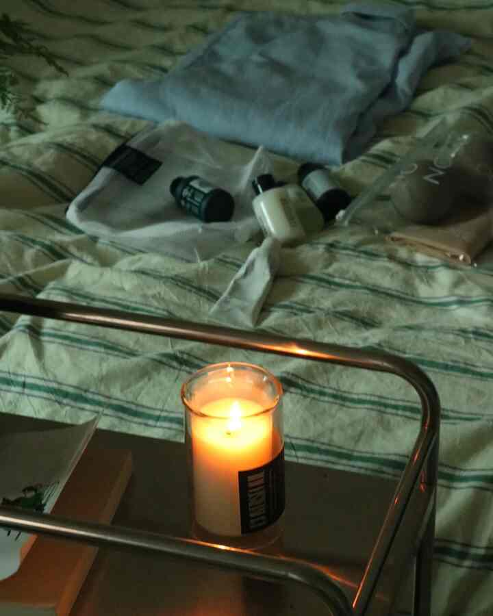 Cozy bedroom with green striped duvet cover featuring a lit candle and cosmetics placed on a stainless steel trolley