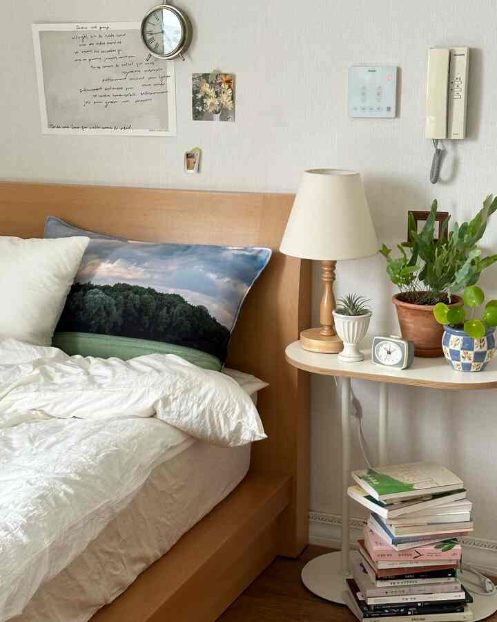 Natural modern bedroom with wood tone bed and white bedding, cozy atmosphere featuring bedside table with lamp and plants