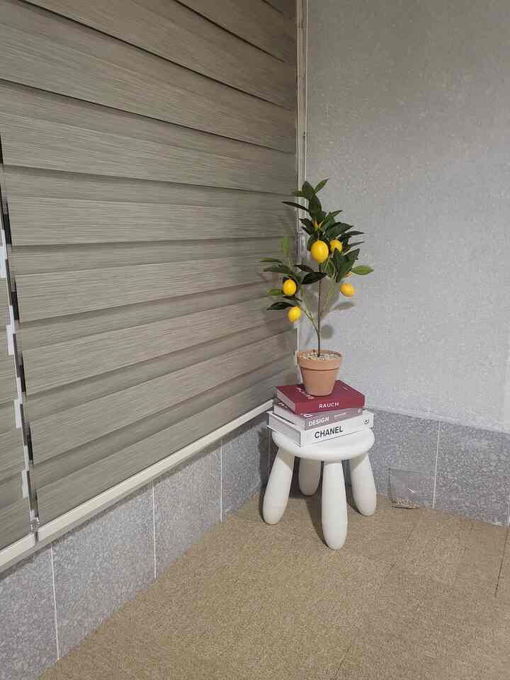 ナチュラルな色調の小さな部屋のコーナー、鉢植えと本が置かれた白いスツールが配置された整った空間