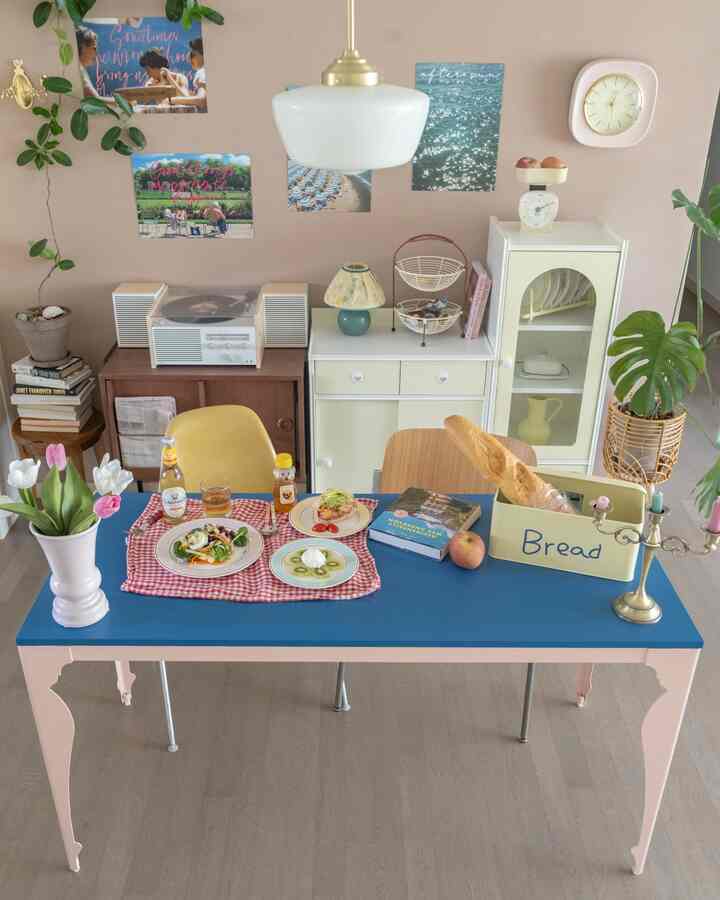 パステルトーンのダイニングルーム、青いダイニングテーブルとヴィンテージ家具、植物が調和した雰囲気のある空間