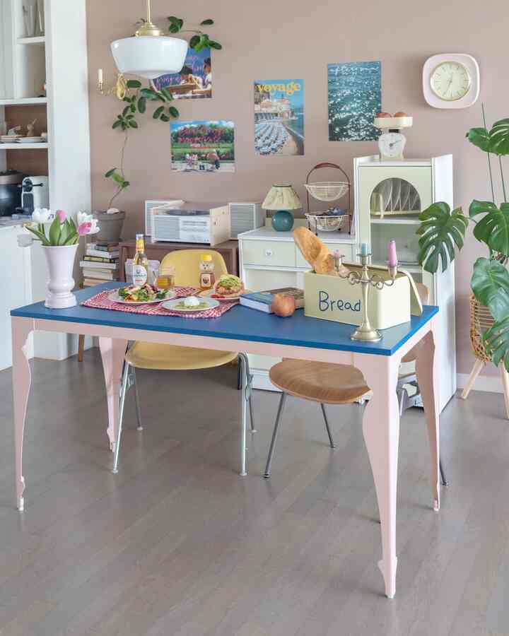 ピンクの壁とブルーのテーブルが調和するダイニング、ヴィンテージの小物とポスターが配置された雰囲気のある空間
