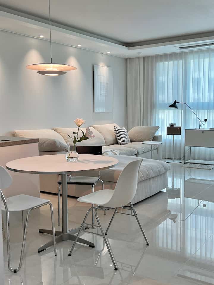 Bright and clean living room featuring white and cream tones, a round dining table, and modern sofa arrangement