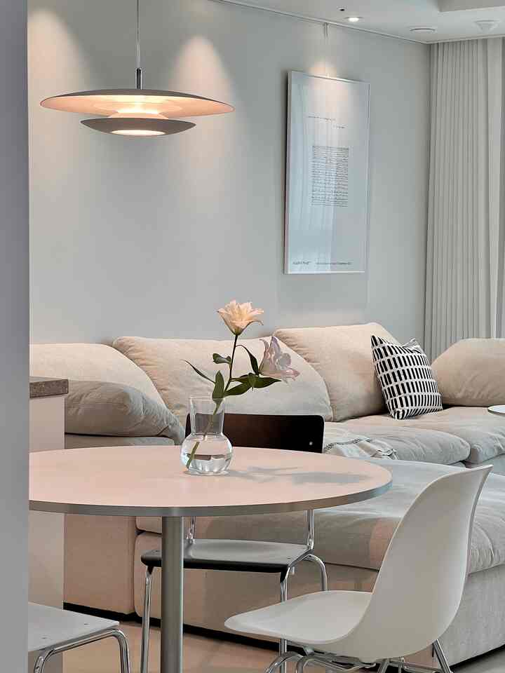 A white and beige toned living room featuring a round table, beige sofa, and pendant light in a clean, modern space