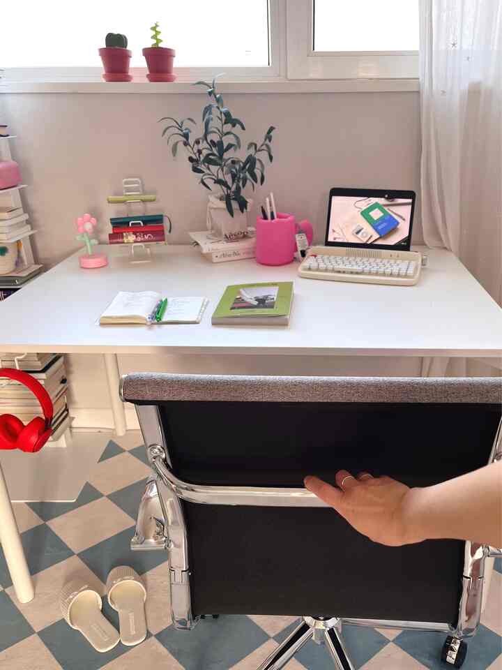 Bright white-toned study space featuring a white desk, black office chair, and plants on the windowsill adding coziness