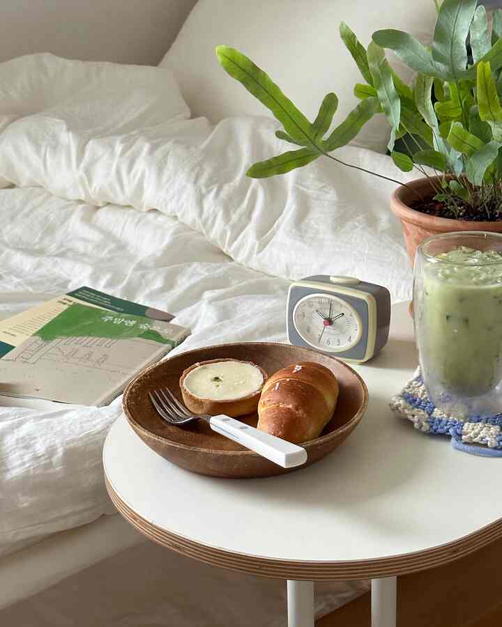 Bright white bedding bedroom featuring a round wood-tone table with green plant for a natural and cozy atmosphere