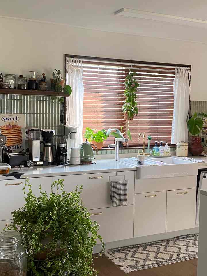 Natural wood tones and white kitchen featuring wooden blinds and plants creating a cozy kitchen space