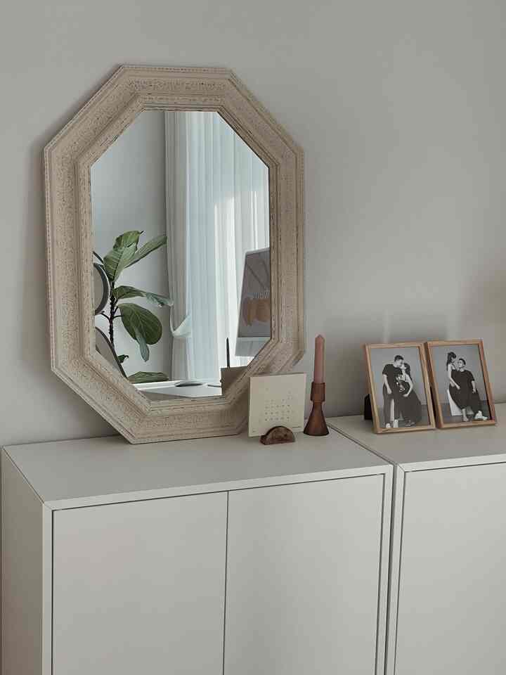 A simple interior space featuring white dressers topped with a vintage-style wooden mirror, candle, and photo frames in wood tones