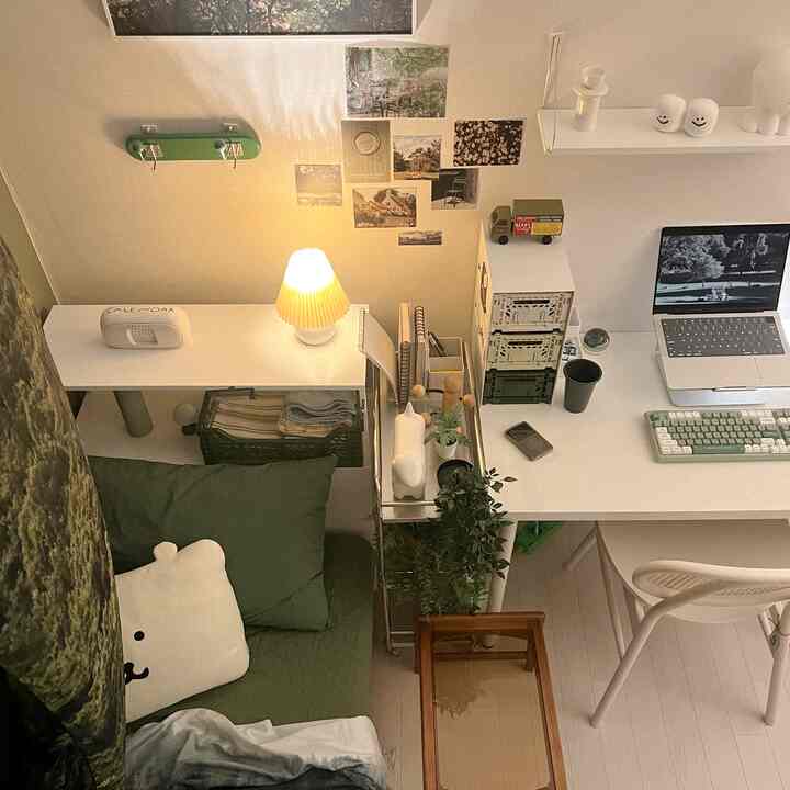白と緑のトーンが特徴の小さなホームオフィス、机と折りたたみ収納ボックス、ソファベッドが配置された居心地の良い一人暮らし向けの空間
