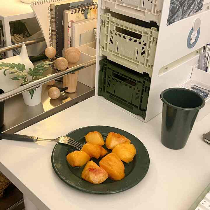 Clean home cafe space on white desk featuring green cup and plate with fruit pieces