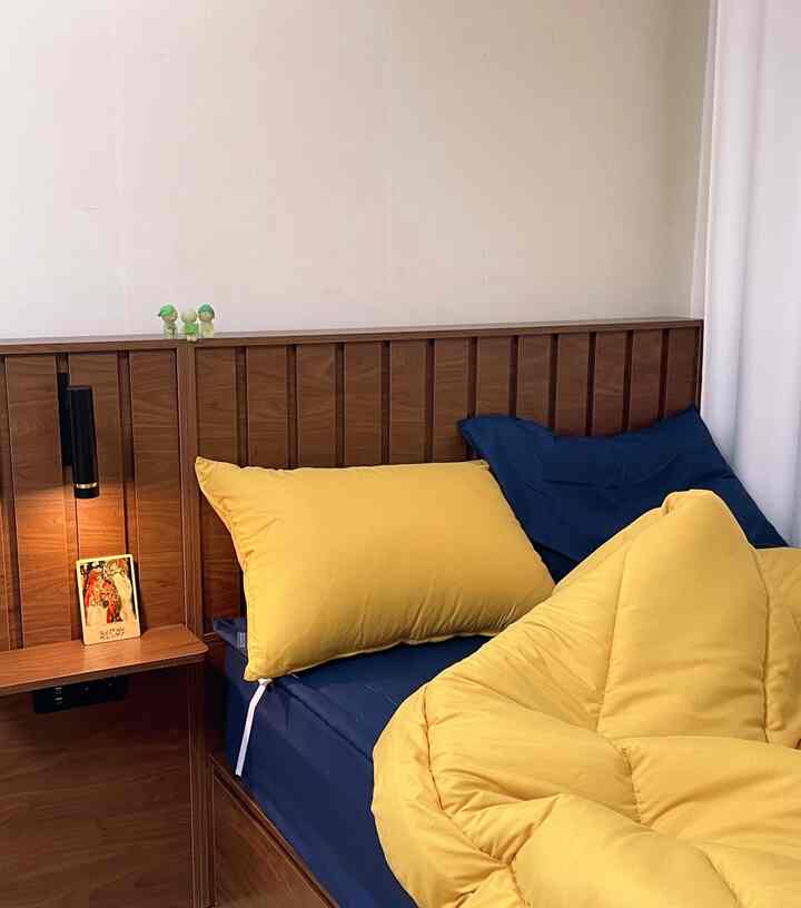 黄とネイビーの寝具と木目調家具が配置されたミッドセンチュリーモダンスタイルの寝室の印象的な空間