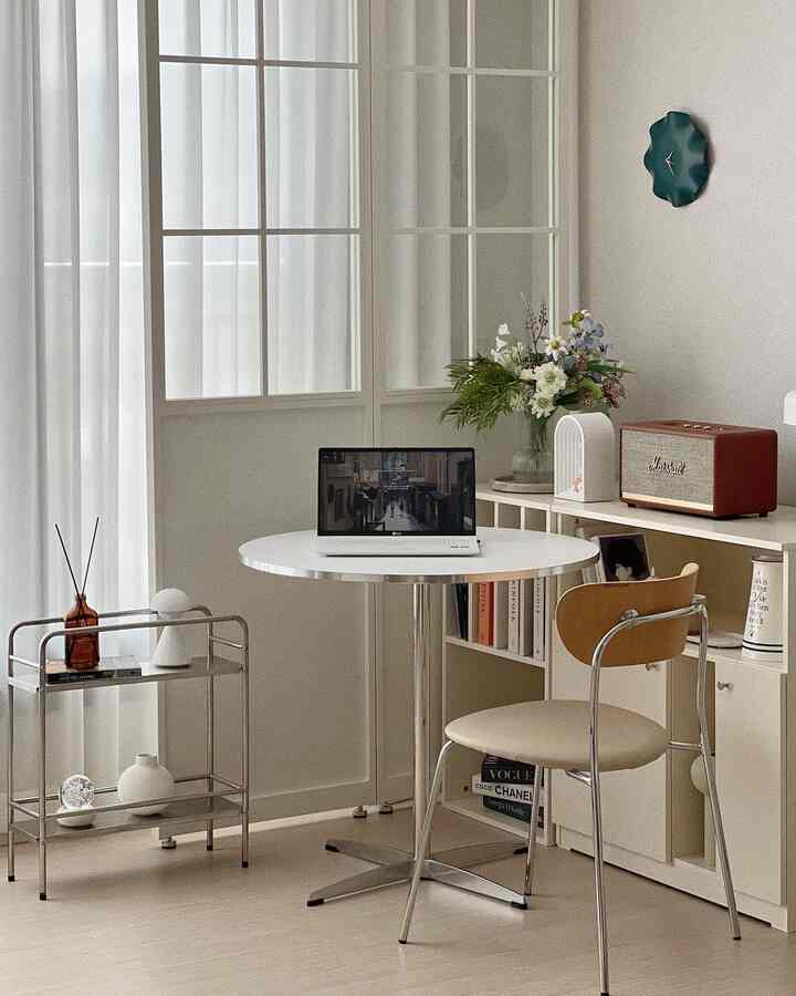 White and beige toned home office space featuring a round table, chair, and bookshelf in a simple interior