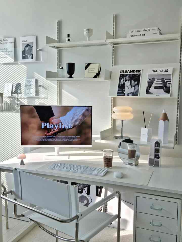 White-toned home office space featuring a white desk, modern chair, wall shelves with diffusers and decor items in a tidy workspace