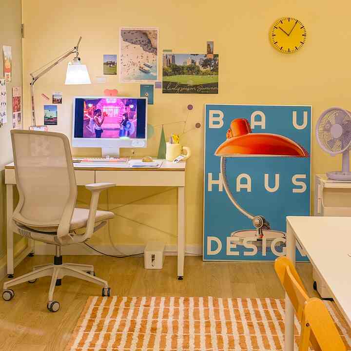Yellow-toned home office space with wood-tone flooring featuring desk, office chair, and decorative posters creating a cozy atmosphere.