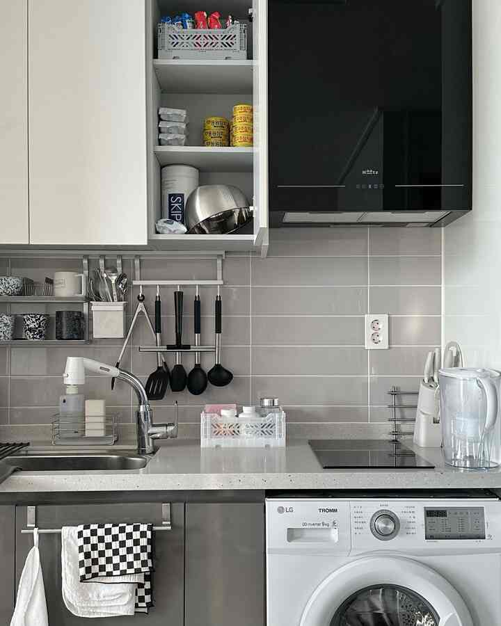 Modern kitchen space featuring gray tiled wall, white upper cabinets, and a black hood
