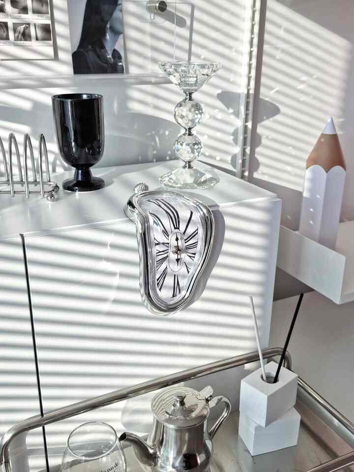 明るい白いトーンのモダンなインテリア空間、中央に溶けるようなデザインの時計と透明なキャンドルホルダーが配置されている