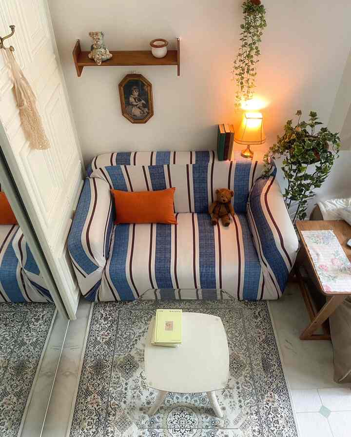 Pastel and wood-tone living room with striped sofa, vintage picture frame, rug, and warm lighting creating cozy atmosphere