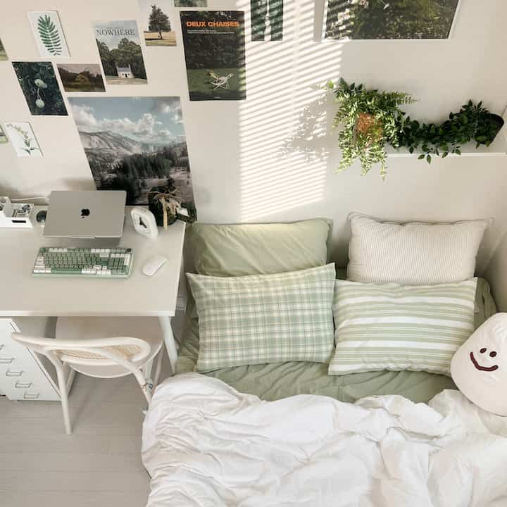 パステルミントとグリーン調の小さな寝室、デスクとベッド、壁のポスターと植物が配置された落ち着いた雰囲気のインテリア