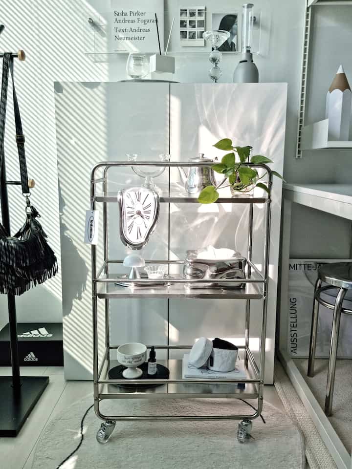 白とシルバーのトーンでまとめられたミッドセンチュリーモダンスタイルのトロリーと小物が配置された明るく整った空間