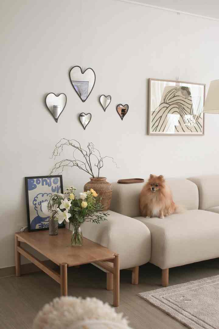 ベージュのソファと木製コーヒーテーブル、ハート形の鏡と額縁アートが配置されたナチュラルな雰囲気のリビング