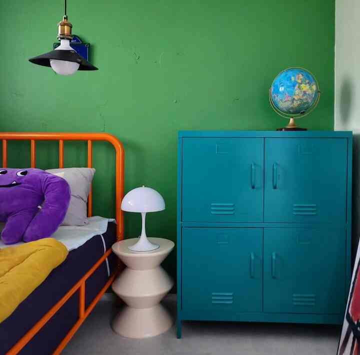 緑色の壁とオレンジ色のベッドフレームがある寝室、青いキャビネットと白いテーブルランプが配置された雰囲気のあるインテリア