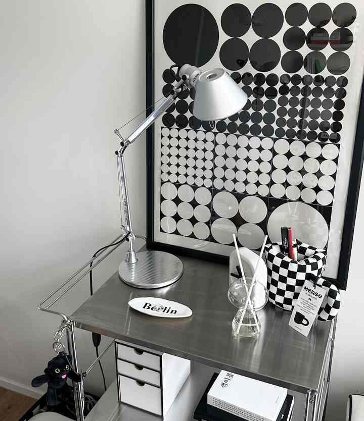 モダンで黒とステンレスのトーンのワンルーム寝室に、ナイトテーブル代わりにステンレストロリーが配置された印象的な空間