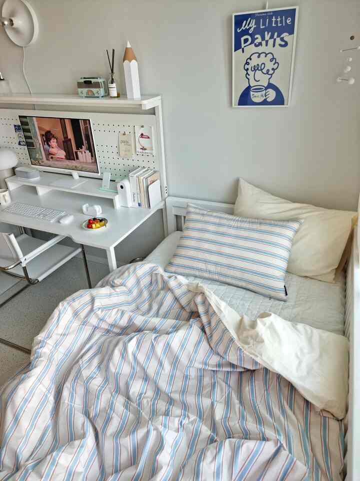 白を基調とした寝室に青のストライプ寝具と白いデスクが配置された雰囲気のあるインテリア