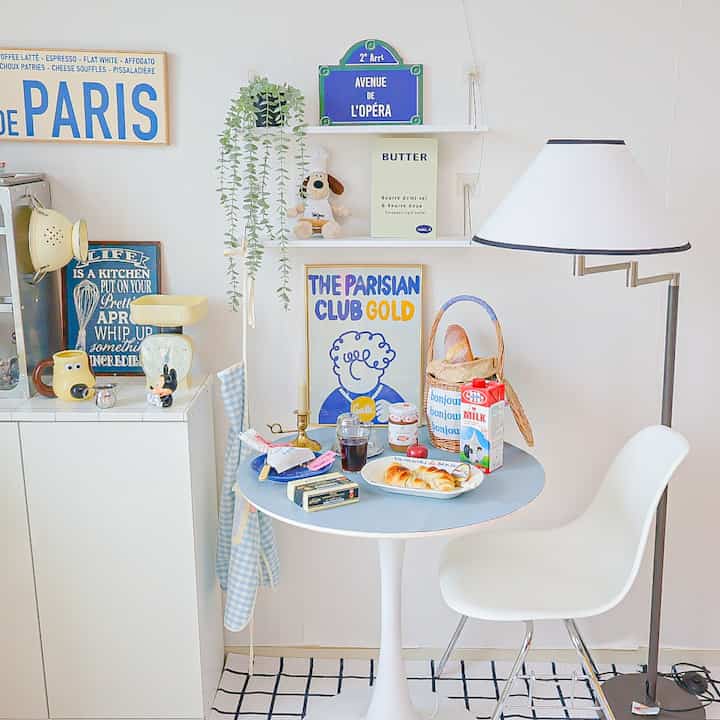 White, blue, and yellow toned kitchen space featuring a small round table, vintage kitchen scale, and wall art creating a simple home cafe style interior