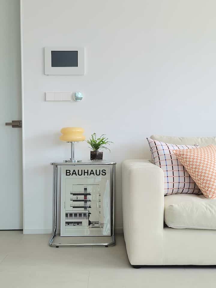 Bright beige and white living room featuring a chrome side table, yellow table lamp, and patterned cushions creating a cozy atmosphere