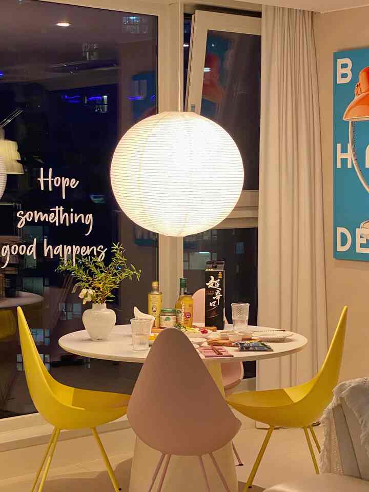 A cozy dining room in white and yellow tones featuring a round table, chairs, and a large spherical pendant light