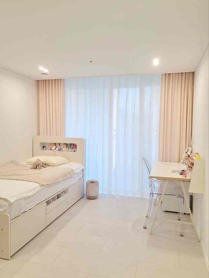 淡いピンクとアイボリーの色調の子供部屋、ベッドとデスク、ピンクのカーテンが温かみのある雰囲気を作り出すインテリア