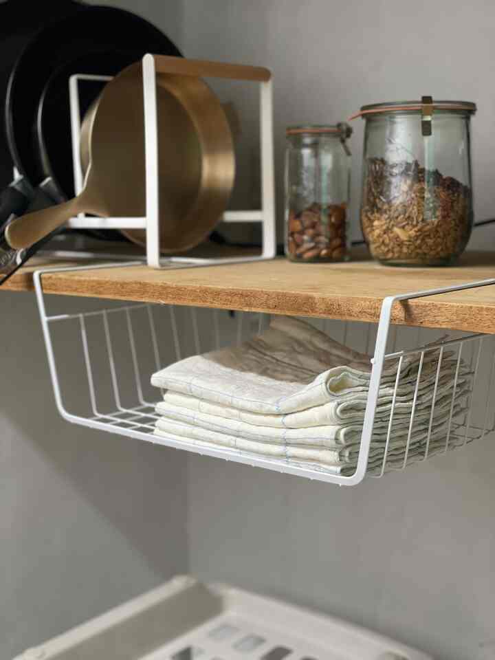 白い金属棚と木目調の棚が配置されたキッチンの隙間収納空間、調理器具やタオルが整然と収納されたミニマルな雰囲気