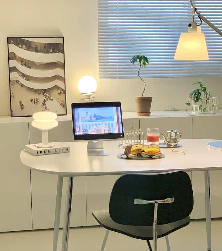 白を基調としたダイニングルーム、中央に白い楕円形のダイニングテーブルと黒い椅子が配置され、照明と植物が調和したモダンなインテリア