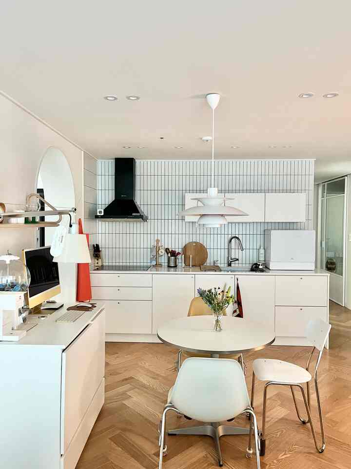 A compact kitchen with white and wood tones featuring a minimal dining table and storage furniture in a clean space