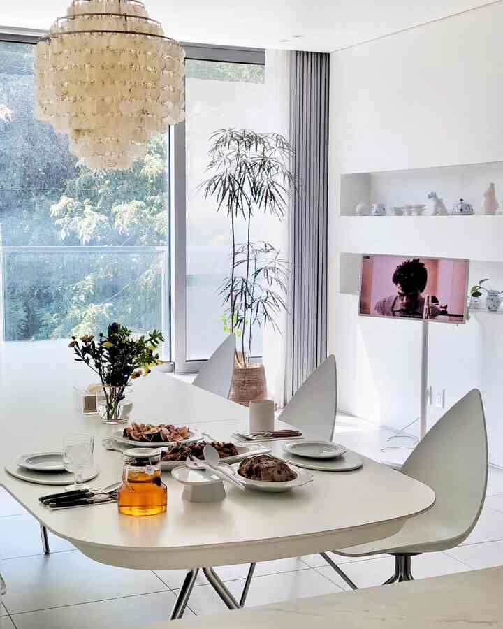 White and charcoal toned dining room featuring a modern dining table and chairs with natural light and a large plant