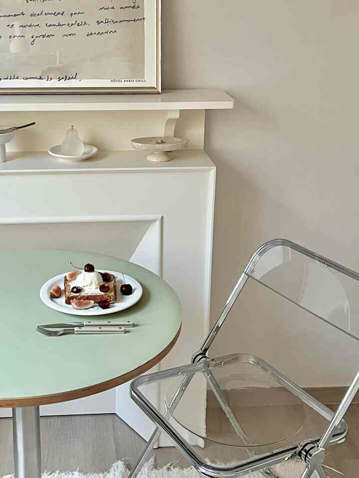 A minimal dining space featuring a pastel green round table with transparent folding chair against beige walls