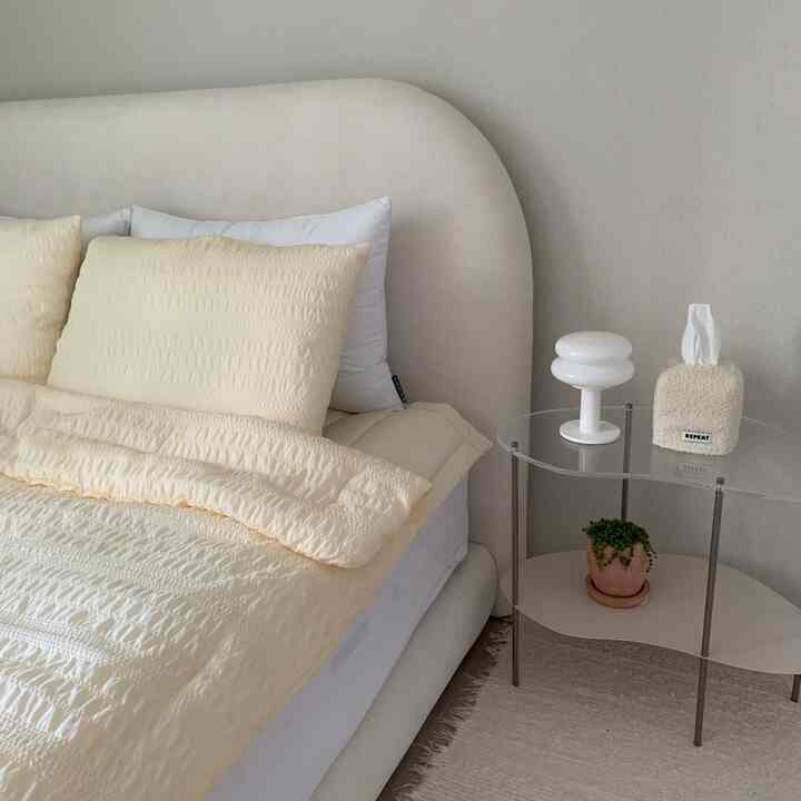 柔らかなベージュとアイボリー調の寝室、アーチ型のベッドフレームと透明なナイトテーブル、シンプルで自然な寝具が配置された雰囲気のあるインテリア