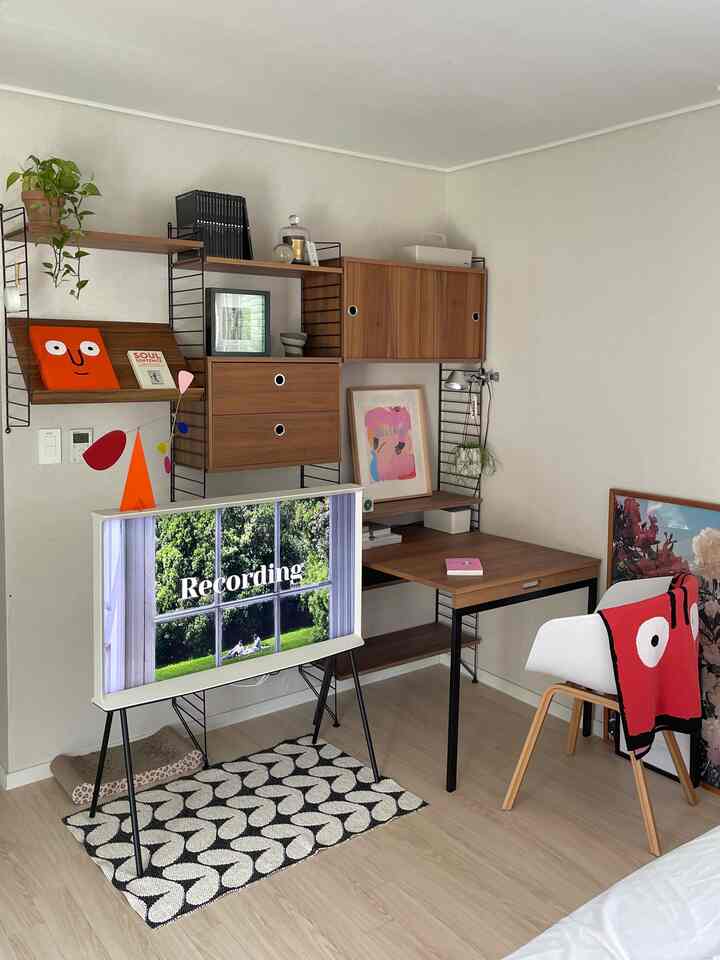 ナチュラルな木目調と白が調和した寝室の一角で、棚やデスク、テレビ台が配置された整ったホームオフィス空間