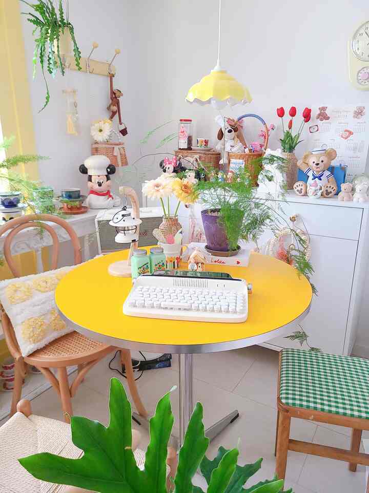 Bright yellow round dining table with white walls in a cozy bedroom home cafe space, styled with plants and vintage decor accents