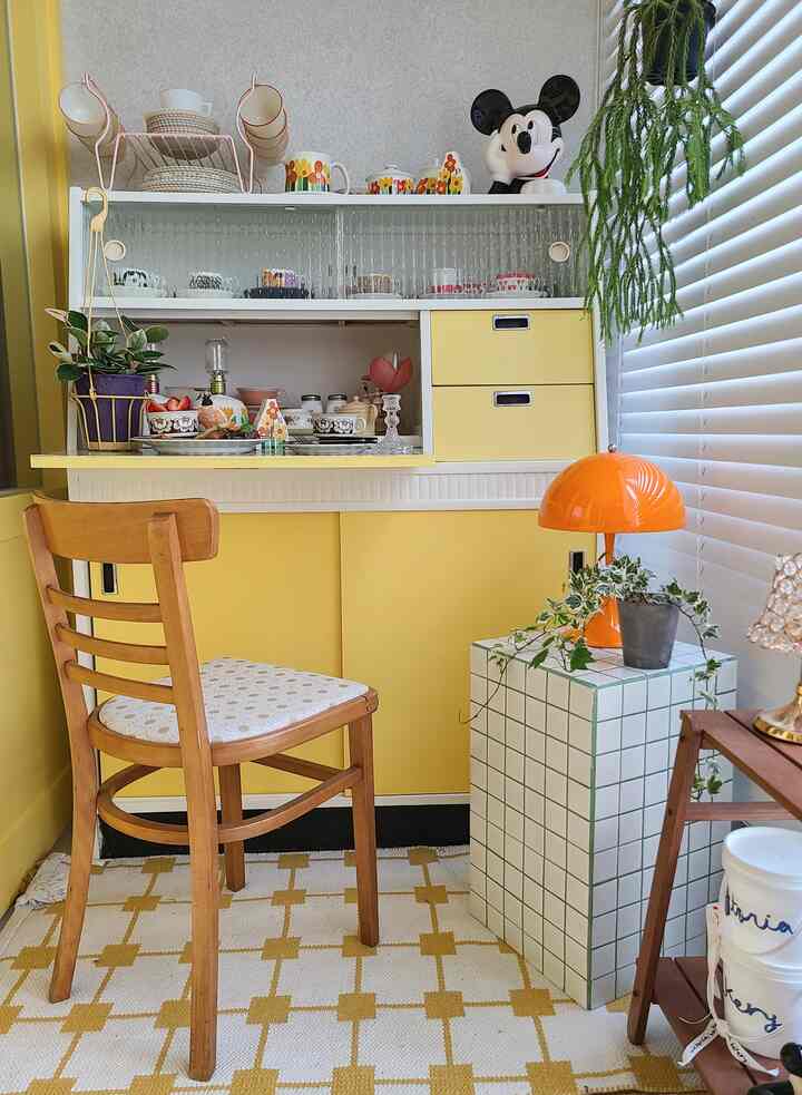 Bright and warm yellow-toned veranda featuring wood tone chair, shelves with cups and decor, giving a cozy home cafe vibe